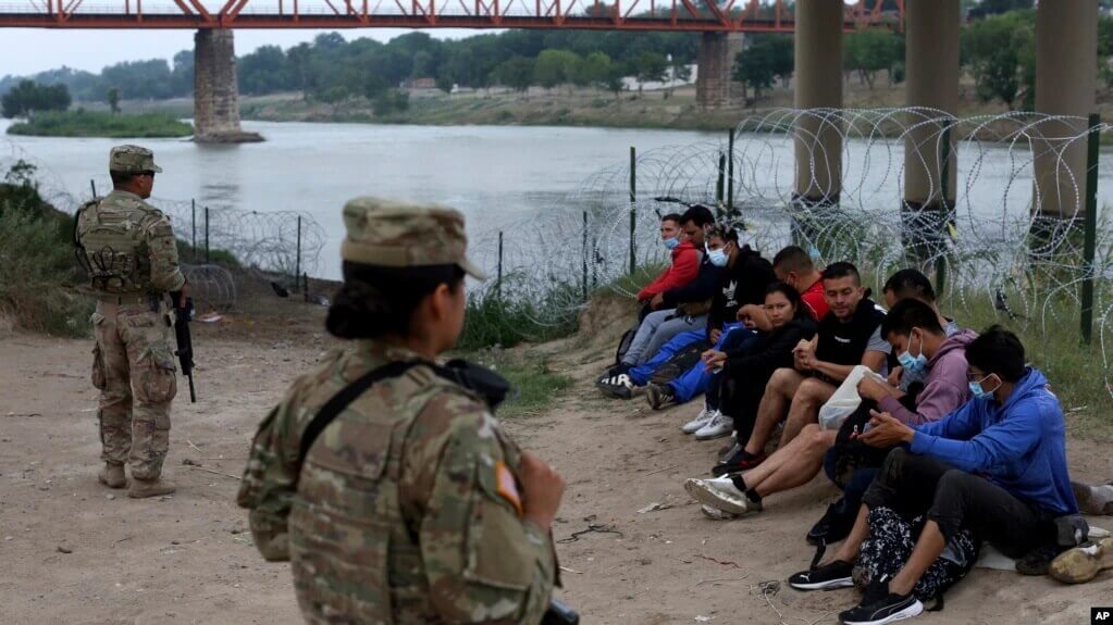 Migrantes que cruzaron el río Bravo hacia EEUU están bajo la custodia de miembros de la Guardia Nacional mientras esperan la llegada de los agentes de la Patrulla Fronteriza EEUU en Eagle Pass, Texas, el viernes 20 de mayo de 2022.