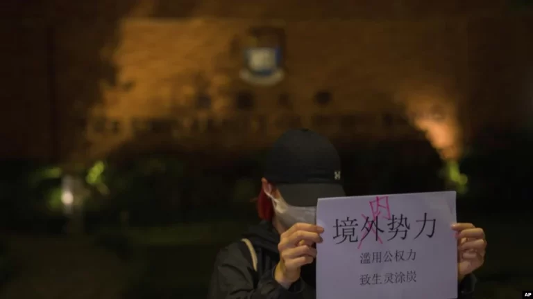 Una manifestante sostiene un cartel con los mensajes "Fuerzas extranjeras no, fuerzas internas" y "El abuso del poder del gobierno hunde a la gente en la miseria y el sufrimiento" durante un encuentro en la Universidad de Hong Kong, el martes 29 de noviembre de 2022.