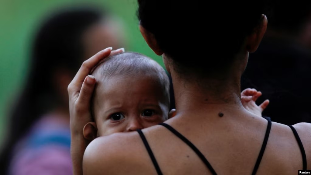 Una mujer migrante sostiene a su hijo mientras los solicitantes de asilo se reúnen para cruzar el río Bravo y entregarse a los agentes de la Patrulla Fronteriza estadounidense antes de que finalice el Título 42, en Matamoros, México, el 10 de mayo de 2023