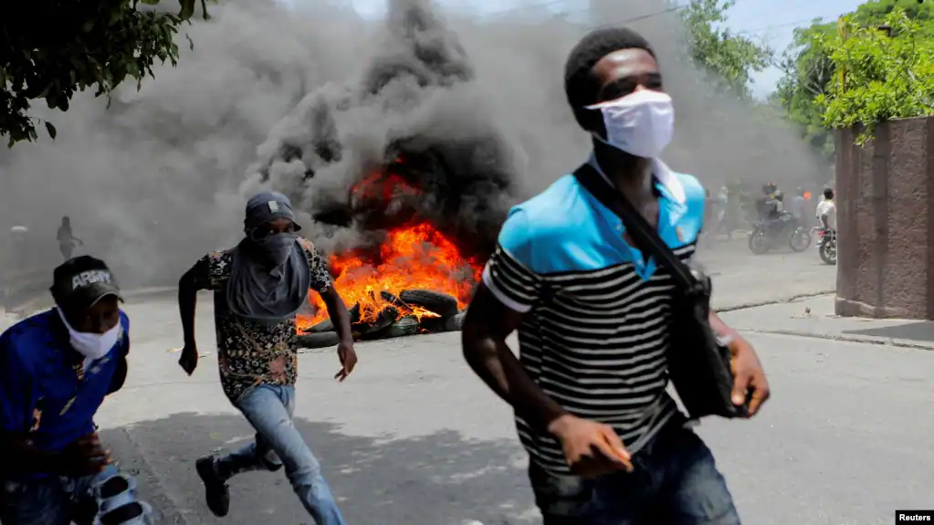 ARCHIVO - Hombres corren junto a neumáticos en llamas durante una protesta que exige el fin de la violencia de las pandillas, en Puerto Príncipe, Haití, el 14 de agosto de 2023.