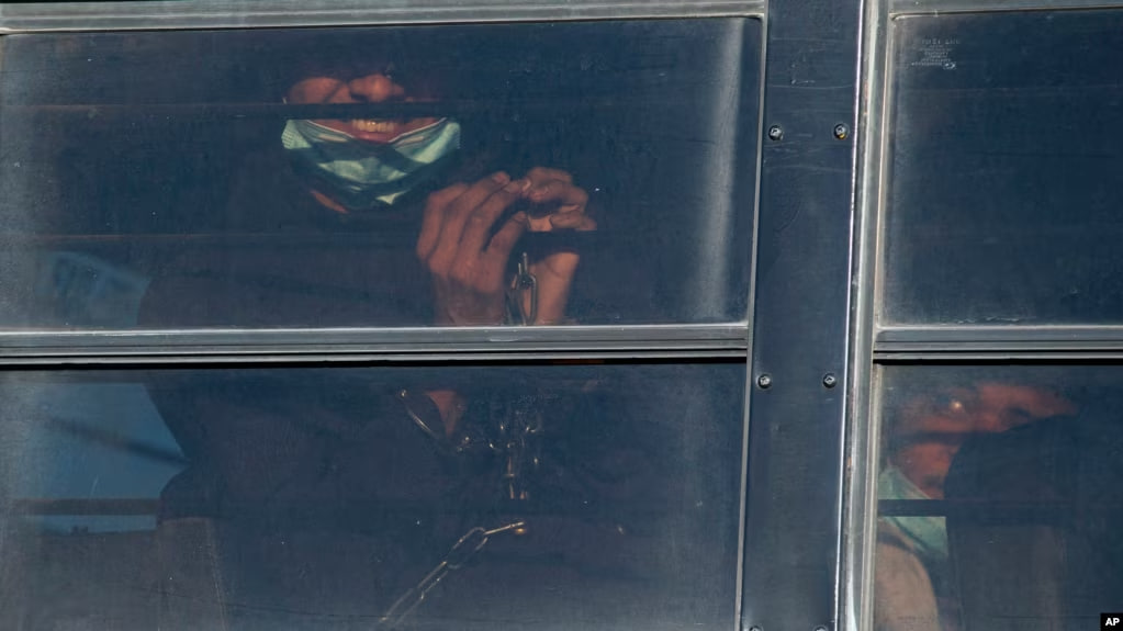 ARCHIVO - Un migrante esposado sonríe mientras es trasladado en autobús para abordar un vuelo de repatriación del Servicio de Control de Inmigración y Aduanas de Estados Unidos hacia Guatemala, el 10 de mayo de 2023, en El Paso, Texas.