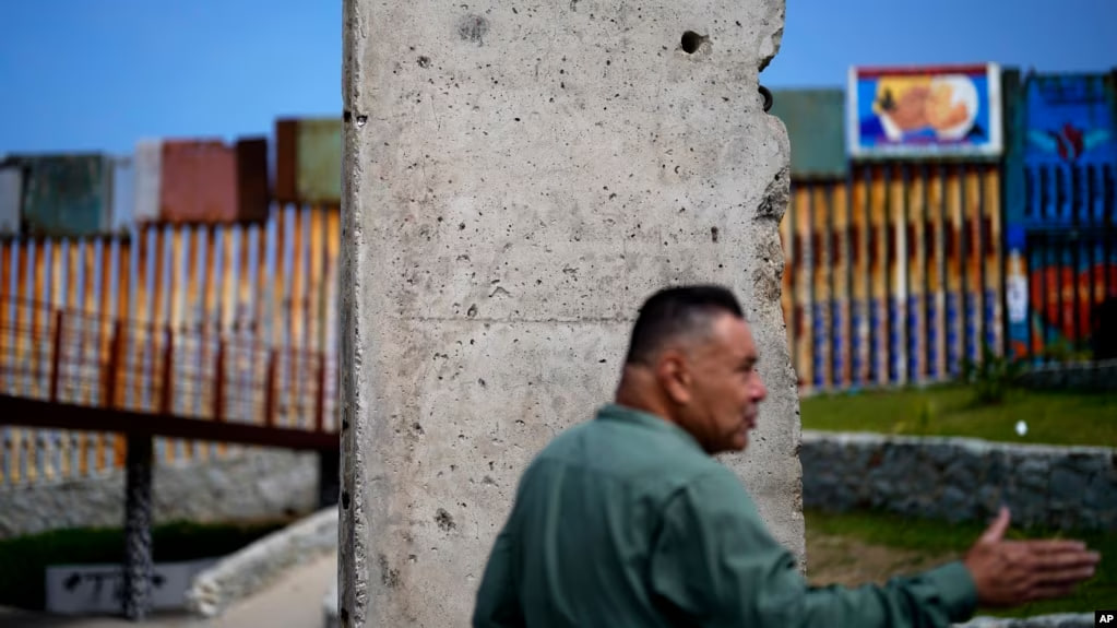 Thomas Correa, del norte de California, habla mientras está parado frente a un remanente del Muro de Berlín, que se encuentra cerca del muro que separa a Estados Unidos de México, en Tijuana, México, el viernes 25 de agosto de 2023.