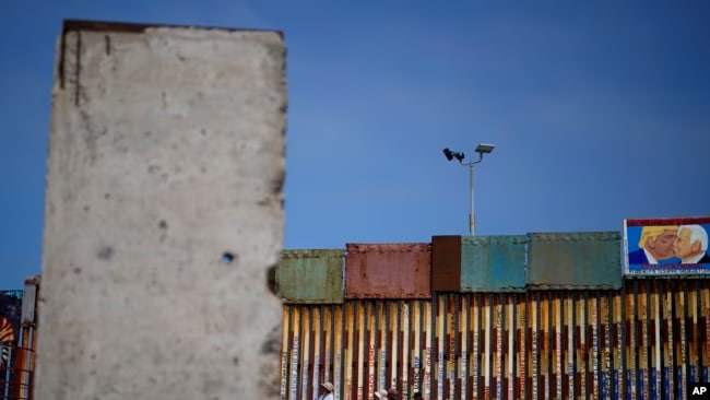 La gente camina a lo largo del muro que separa Estados Unidos de México, cerca de una losa del Muro de Berlín, en Tijuana, México, el viernes 25 de agosto de 2023.