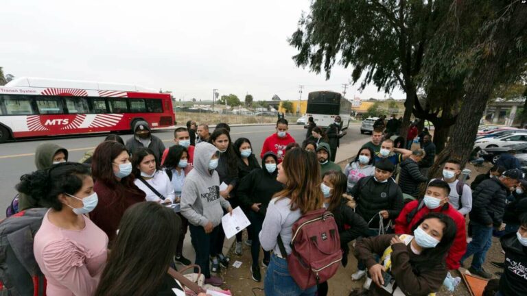 Migrantes escuchan a un voluntario en un estacionamiento después de ser detenidos y procesados ​​para solicitar asilo por parte de Estados Unidos. autoridades, viernes 12 de abril de 2024, en San Diego.